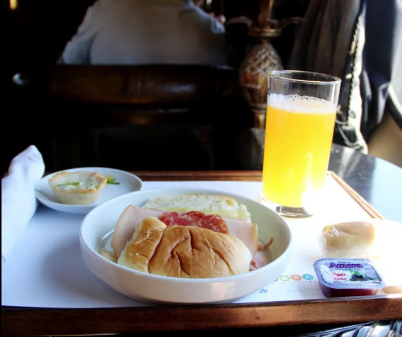 Kit lanche servido na primeira classe do trem com croissant e bebidas.